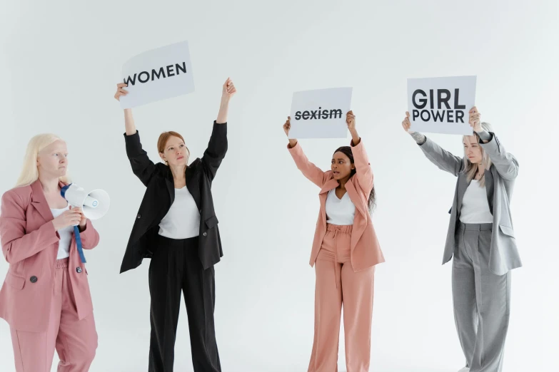 a group of women standing next to each other holding signs, a cartoon, trending on pexels, hypermasculine, on grey background, feminism, background image