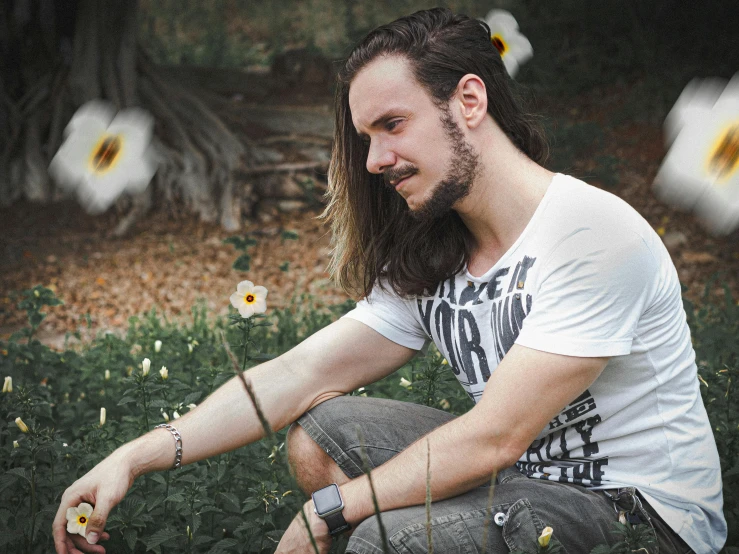 a man with long hair sitting in a field of flowers, dressed in a white t shirt, profile image, trending photo, avatar image