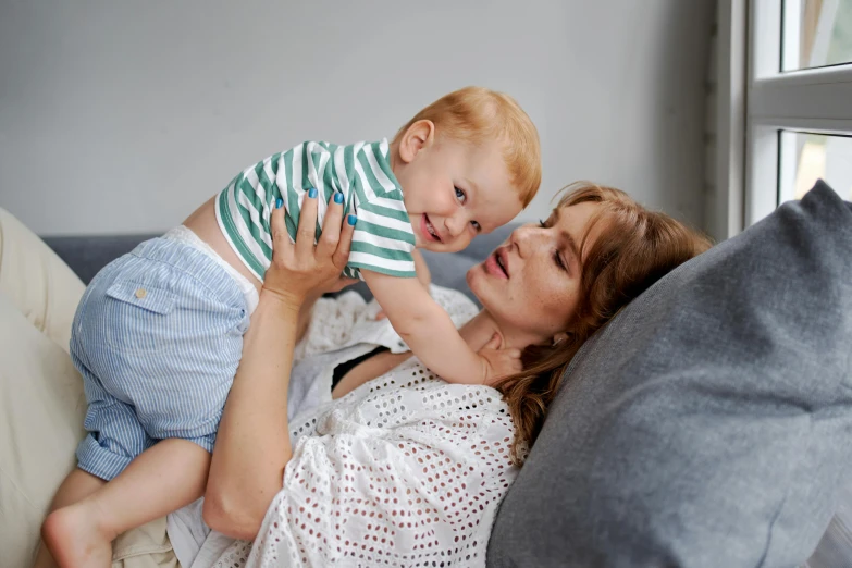 a woman laying on a couch holding a baby, pexels contest winner, happening, brunette boy and redhead boy, thumbnail, super high resolution, looking her shoulder