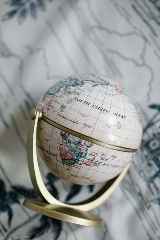 a small globe sitting on top of a bed, up-close, product shot, round-cropped, cartography