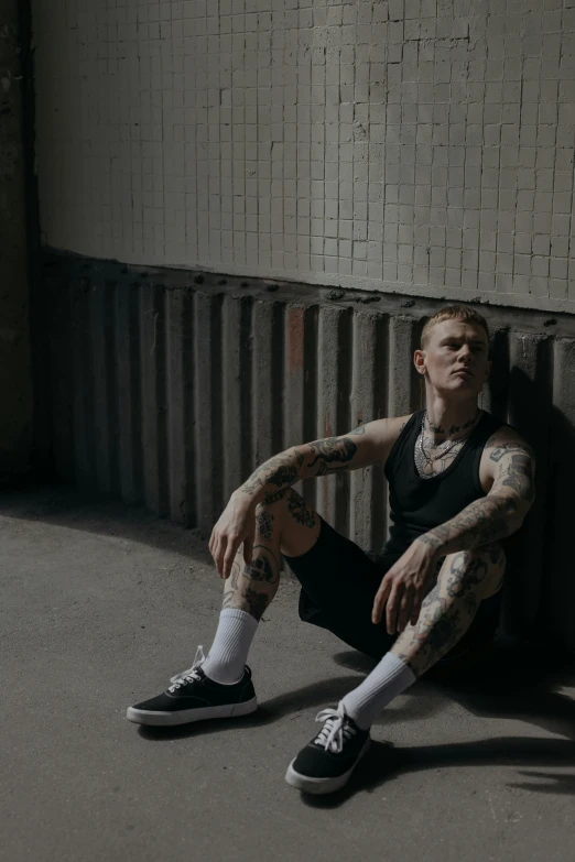 a man with tattoos sitting against a wall, inspired by Seb McKinnon, pexels contest winner, bauhaus, yung lean, in a warehouse, lean man with light tan skin, soccer players martin ødegaard