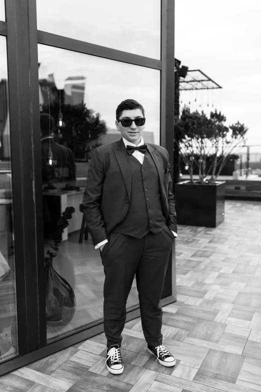 a man in a suit and sunglasses standing in front of a building, a black and white photo, inspired by Dmitry Levitzky, reddit, andy milonakis, standing in a restaurant, pose 4 of 1 6, maxim sukharev