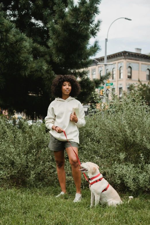 a woman standing next to a white dog on a leash, trending on unsplash, renaissance, lush brooklyn urban landscaping, wearing an oversized hoodie, african american young woman, dressed in a top and shorts