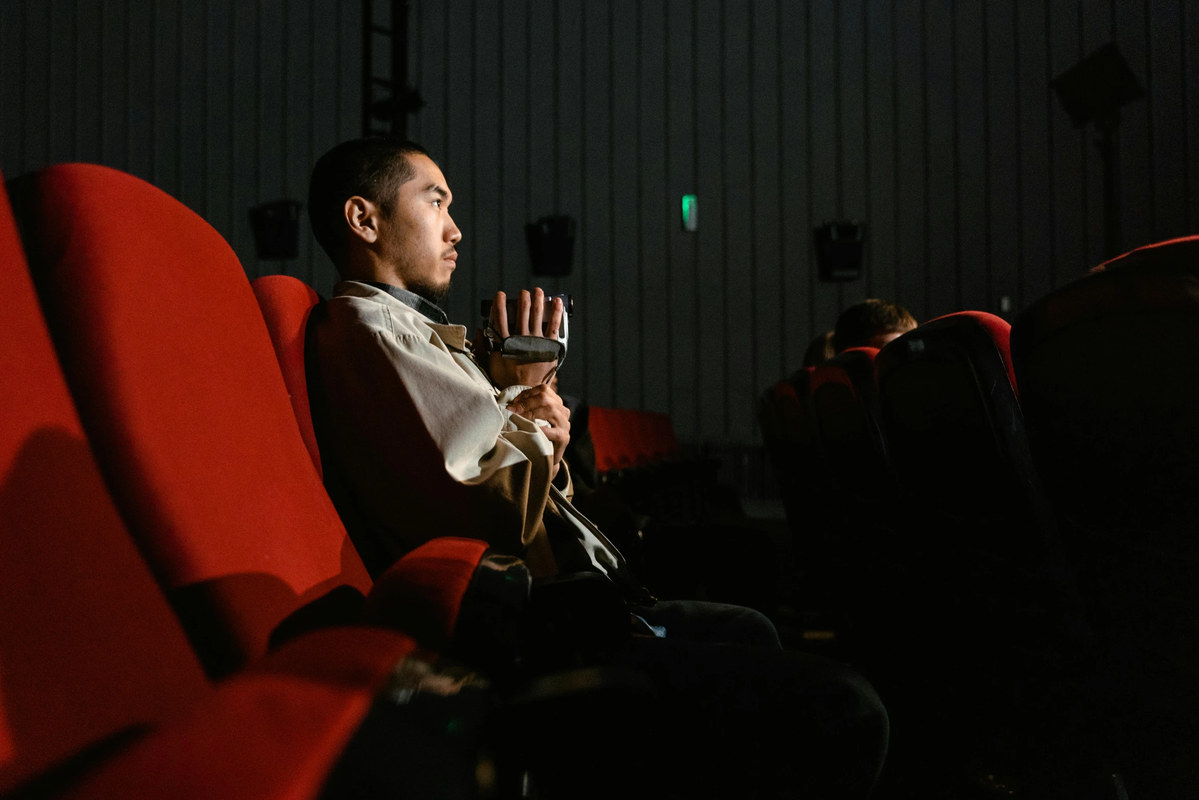 a man sitting in a movie theater holding a remote control, inspired by Fei Danxu, unsplash, video art, sitting on a chair, cai xukun, [ theatrical ], multiple stories