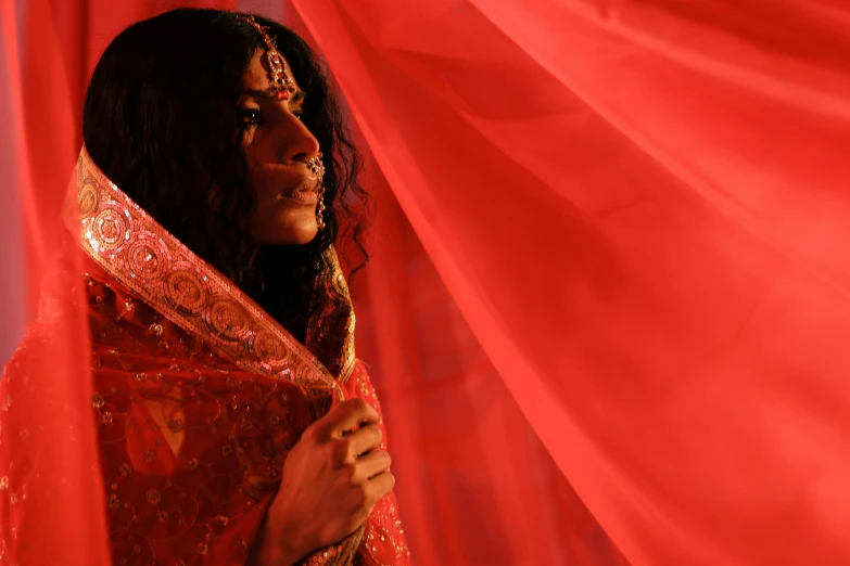 a woman is hiding behind a red cloth, an album cover, pexels contest winner, transgressive art, dressed in a sari, [ theatrical ], lgbtq, perfectly lit. movie still