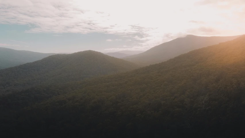 the sun shines through the clouds over the mountains, a picture, unsplash contest winner, australian tonalism, overlooking a vast serene forest, movie still 8 k, drone footage, instagram picture