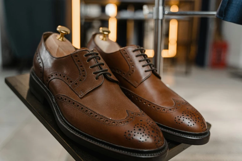 a pair of brown shoes sitting on top of a wooden table, inspired by Barthélemy Menn, hurufiyya, chesterfield, exceptional, pièce de résistance, features