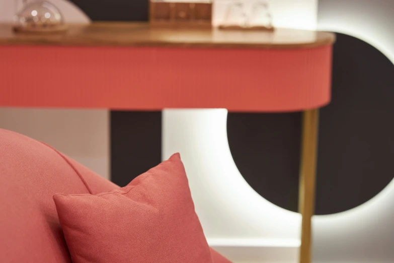 a pink couch sitting in a living room next to a table, inspired by Joseph Wright of Derby, light and space, lacquered oak reception desk, coral red, medium close up shot, curved