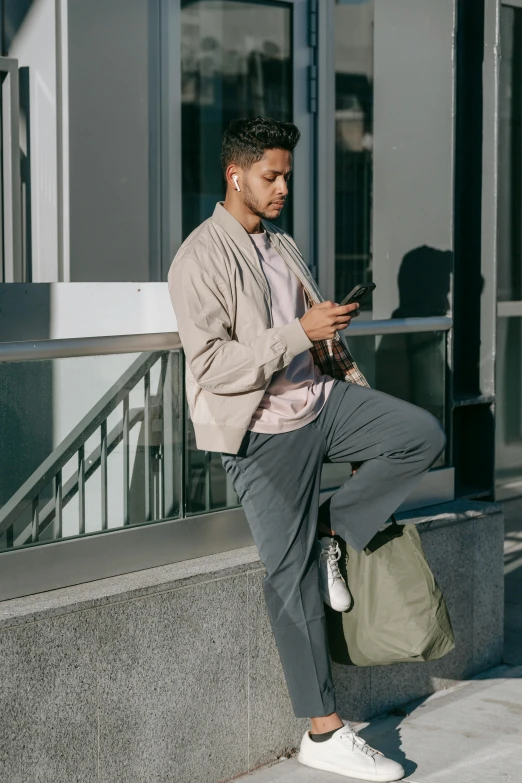 a man sitting on a ledge looking at his cell phone, by Cosmo Alexander, trending on pexels, renaissance, olive green slacks, dressed in a gray, bag over the waist, full body full height