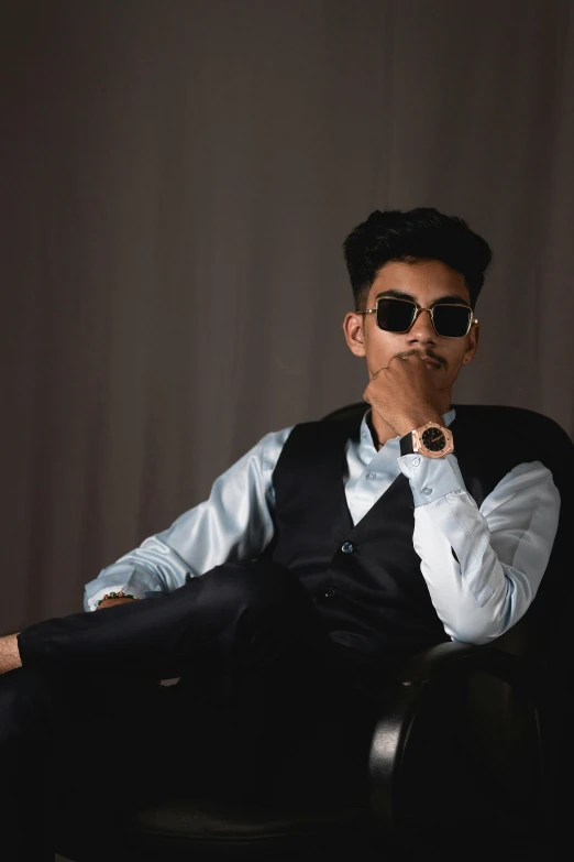 a man sitting in a chair smoking a cigarette, an album cover, inspired by Rudy Siswanto, trending on unsplash, sumatraism, formal wear, wear ray - ban glass, androgynous, model posing