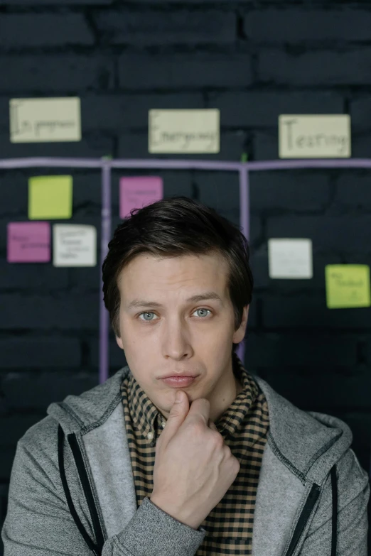 a man standing in front of a wall with sticky notes on it, a poster, inspired by Oskar Lüthy, androgynous person, looking serious, still from a movie, young adult