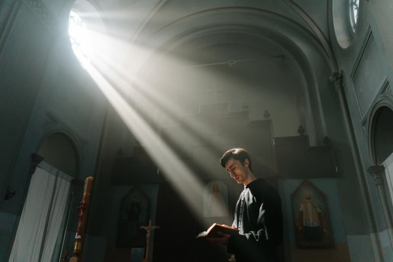 a man standing in a church reading a book, pexels contest winner, light and space, orthodox saint, lights beam, instagram post, [ cinematic