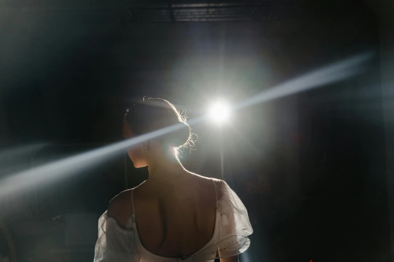 a woman in a white dress standing in a dark room, light and space, dramatic lens flares, ballet performance photography, the sun at their back, pictured from the shoulders up