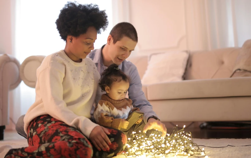 a couple of people that are sitting on the floor, pexels, christmas lights, portrait of family of three, avatar image, natural light