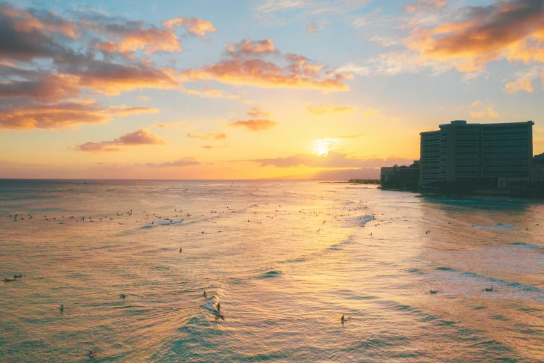 a group of people riding surfboards on top of a large body of water, by Carey Morris, pexels contest winner, fine art, waikiki beach skyline, which shows a beach at sunset, sunfaded, bird's eye