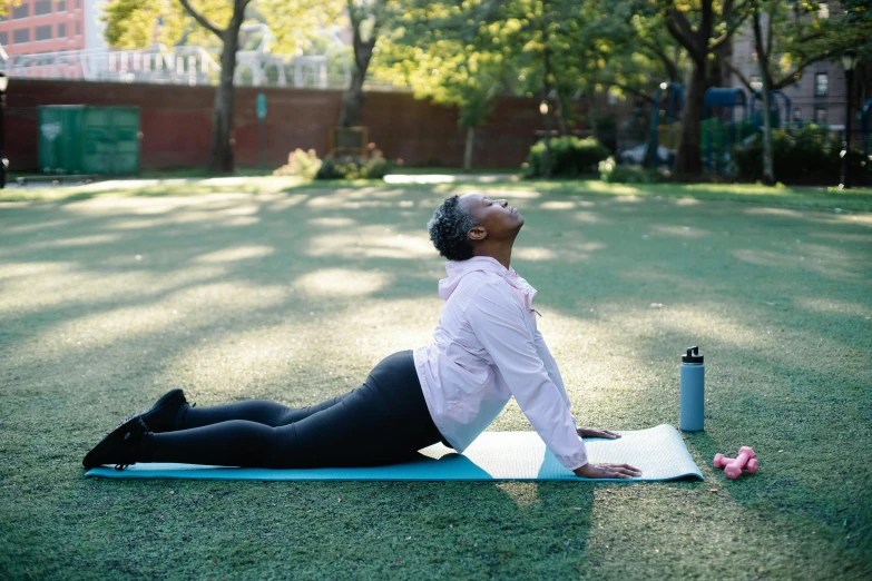 a woman sitting on a yoga mat next to a water bottle, pexels contest winner, figuration libre, stretching her legs on the grass, arched back, photo of a black woman, pictured from the shoulders up