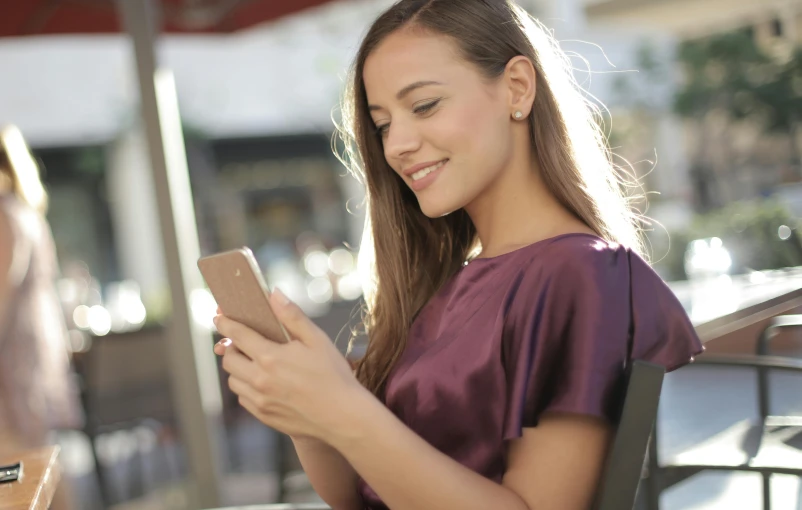 a woman sitting at a table using a cell phone, trending on pexels, happening, avatar image, outside, brown, good looking