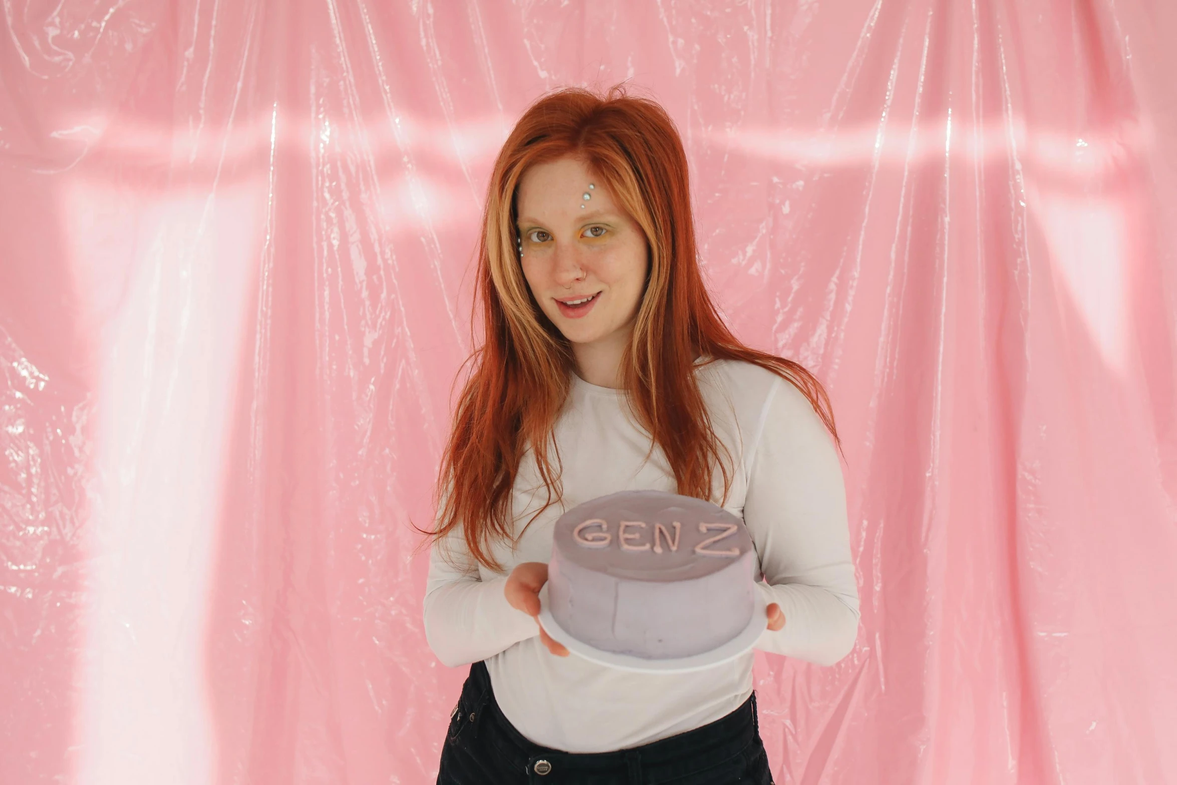 a woman holding a cake in front of a pink backdrop, an album cover, by Grace Clements, she has long redorange hair, on a white table, slightly holographic, gen z