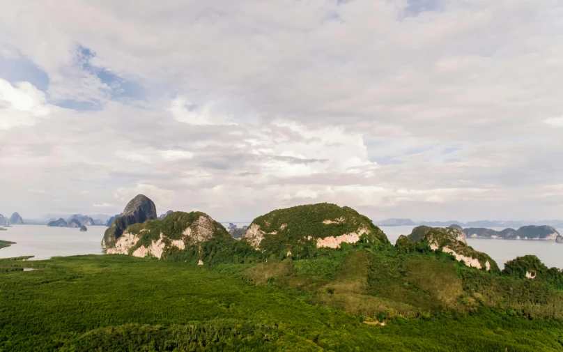 a large body of water sitting on top of a lush green hillside, an album cover, pexels contest winner, sumatraism, limestone, two mountains in background, 4 k cinematic panoramic view, flying above a tropical forest