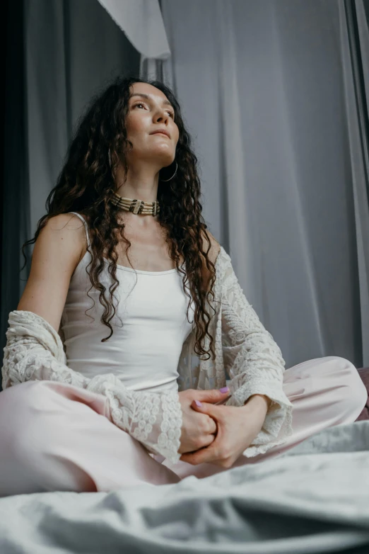 a woman in a white top and pink pants sitting on a bed, by Ivana Kobilca, trending on pexels, renaissance, long dark curly hair, a cyborg meditating, profile image, concert