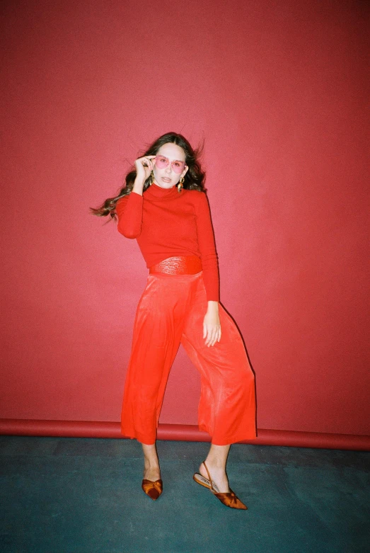 a woman standing in front of a red wall, wearing a red outfit, wearing pants, lily frank, hazy