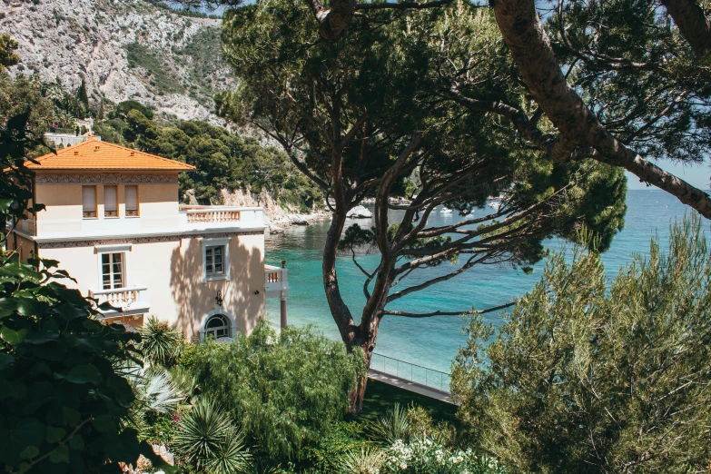 a house sitting on top of a lush green hillside, inspired by Jean-Yves Couliou, pexels contest winner, les nabis, next to the sea, calanque, wes anderson), beach trees in the background