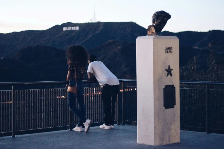 a couple of people standing next to a statue, pexels contest winner, mulholland drive, sza, ☁🌪🌙👩🏾, view from the side