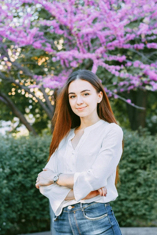 a woman standing in front of a tree with purple flowers, wearing a light shirt, yulia nevskaya, at college, portrait image