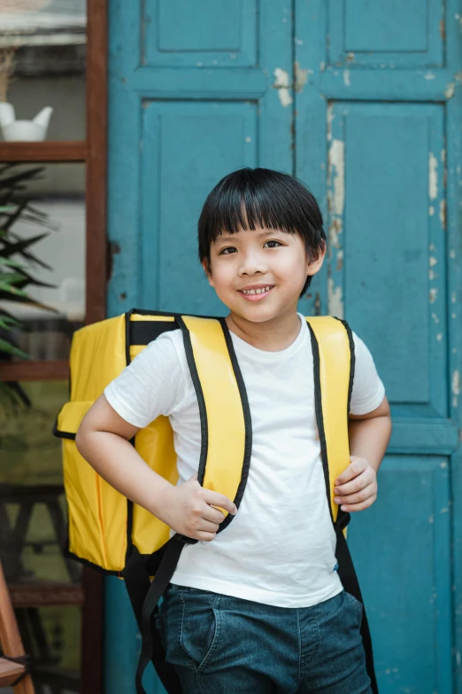 a young boy standing in front of a blue door, pexels, happening, square backpack, wearing a modern yellow tshirt, wearing japanese school uniform, ad image