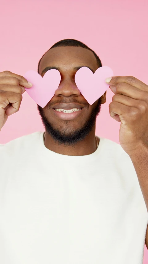 a man holding two pink hearts in front of his eyes, trending on pexels, black man, cute slightly nerdy smile, lgbt, essence