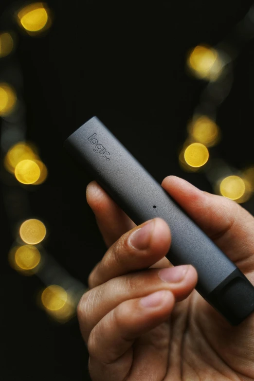 a person holding an electronic device in their hand, tachisme, holding a small vape, black matte finish, holiday vibe, lit from bottom