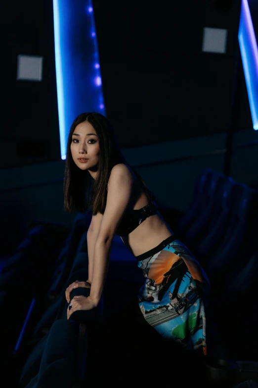 a woman sitting on a chair in a dark room, an album cover, inspired by Feng Zhu, unsplash, holography, standing in a starbase bar, bare midriff, li bingbing, gemma chan girl portrait