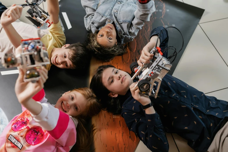 a group of children sitting on top of a wooden floor, robotics, avatar image, lego, drone photograph