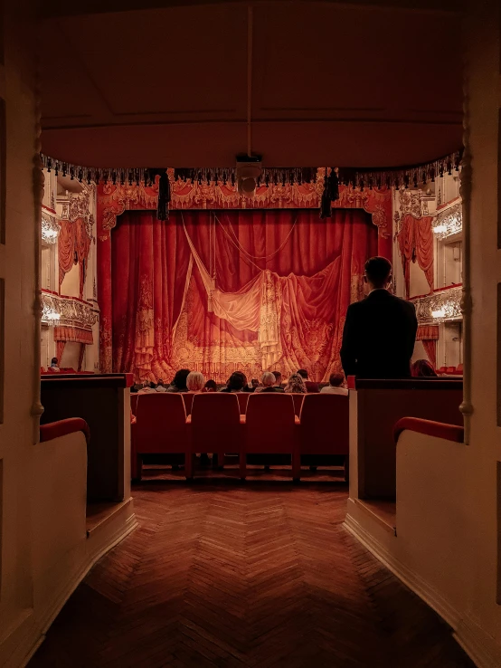 a couple of people that are sitting in front of a stage, by Elsa Bleda, unsplash contest winner, baroque, theater curtains are red, soviet interior, profile image, cinemascope panorama