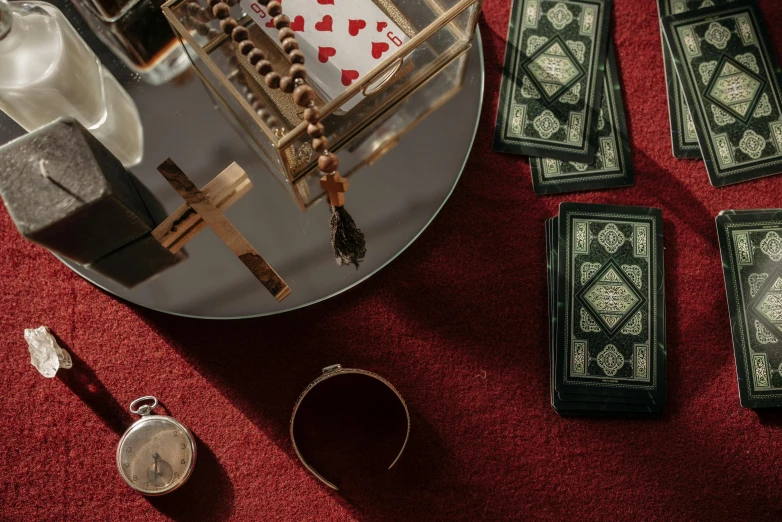 a table topped with lots of cards on top of a red carpet, a still life, by Julia Pishtar, trending on pexels, mirror and glass surfaces, wearing gothic accessories, game and watch, alessio albi