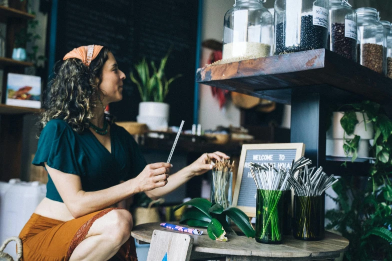 a woman sitting on a stool in a flower shop, unsplash, holding magical kitchen knives, aussie baristas, avatar image, with a straw