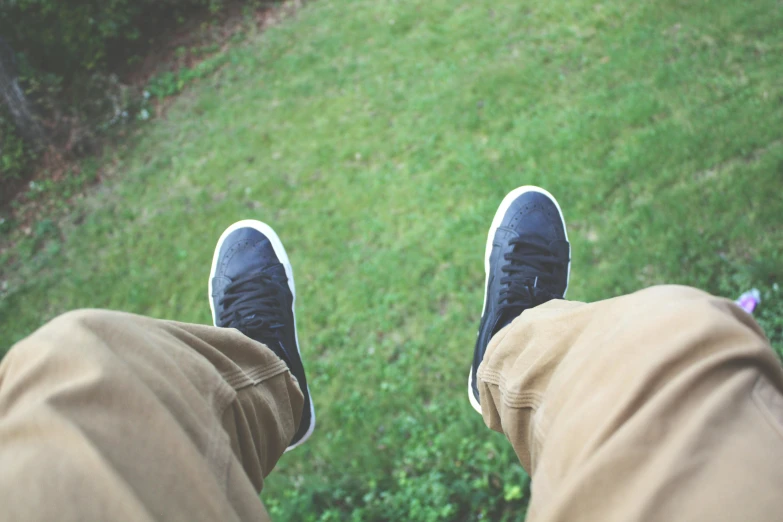 a person standing on top of a lush green field, a picture, happening, sneakers, wearing pants, looking up at camera, leg high