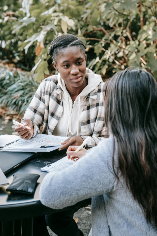 two women sitting at a table talking to each other, pexels contest winner, academic art, in a park, african american young woman, selling insurance, document photo