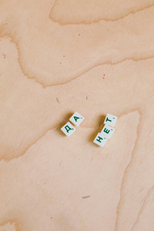 a couple of scrabbles sitting on top of a wooden table, unsplash, visual art, emerald earrings, say ahh, akt photography, concrete poetry