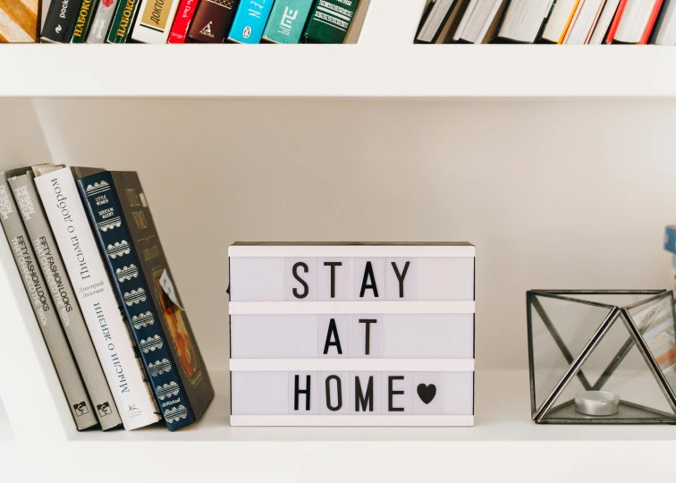 a shelf with books and a sign that says stay at home, unsplash, lit. 'the cube', fully decorated, profile image, frontal shot