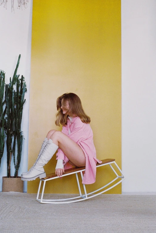 a woman sitting on a rocking chair next to a cactus, an album cover, trending on pexels, knee-high boots, white and light-pink outfit, britt marling style, yellow clothes