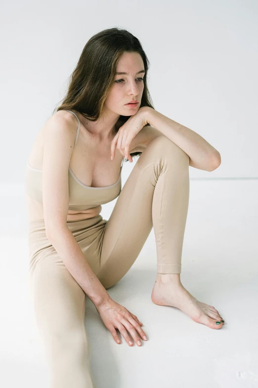 a woman sitting on top of a white floor, wearing tight simple clothes, light tan, with pale skin, louise zhang