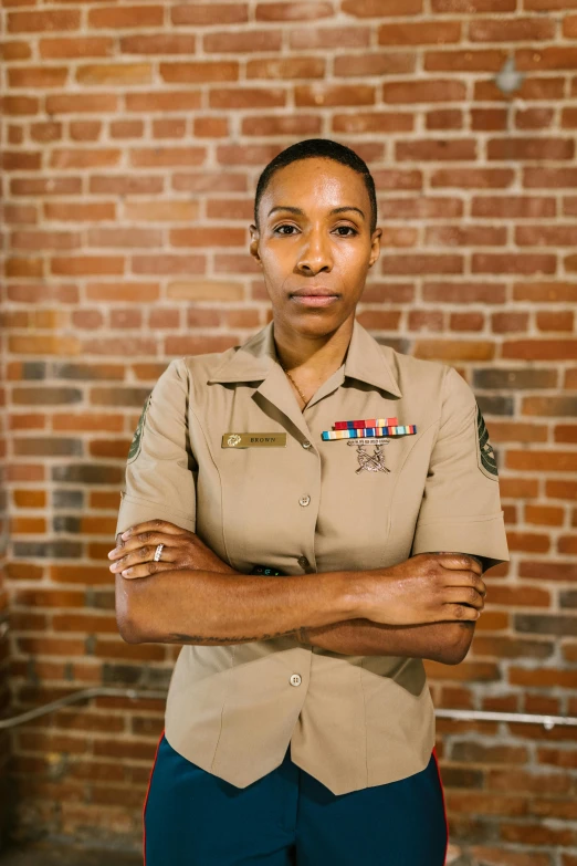 a woman in uniform standing in front of a brick wall, by Alison Geissler, ashteroth, looking serious, marine, slide show