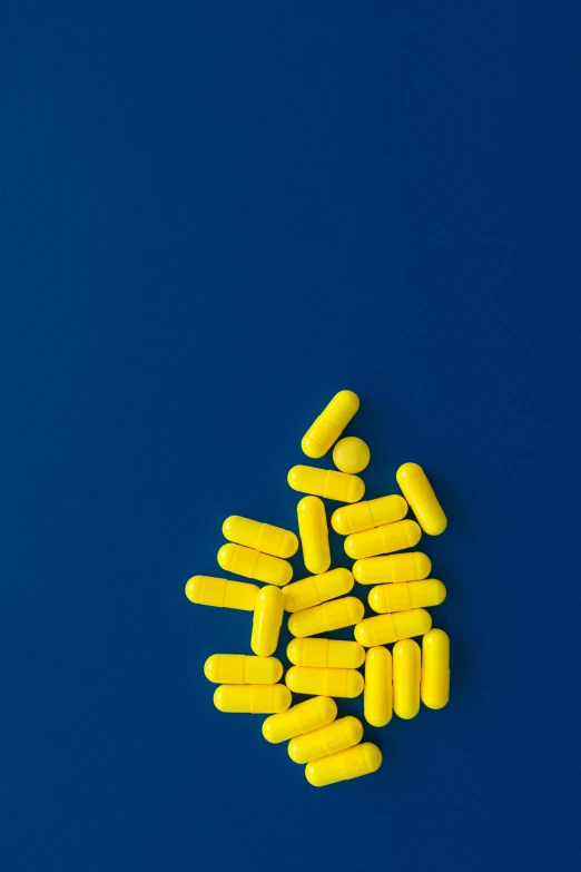 a pile of yellow pills on a blue background, inspired by Yves Klein, unsplash, full body image, strokes, alien capsules, hcl