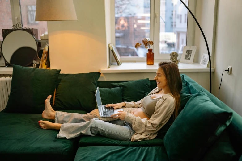 a woman sitting on a green couch using a laptop, pexels contest winner, third trimester, open plan, couches vibrating and melting, green corduroy pants