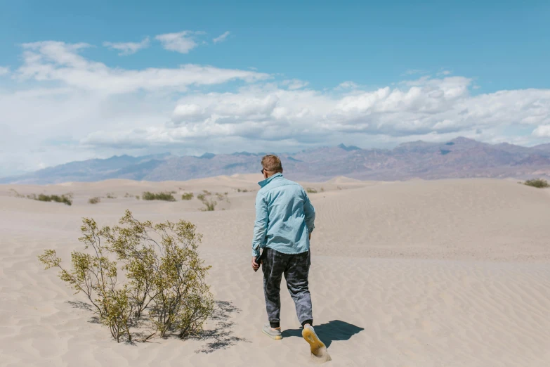 a man standing in the middle of a desert, wearing a blue jacket, on a canva, sand banks, death valley
