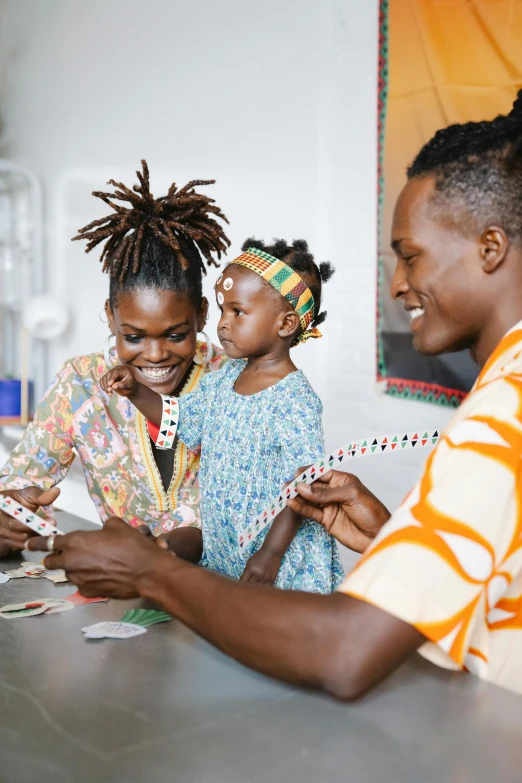a group of people sitting at a table playing cards, a picture, by Ingrida Kadaka, pexels contest winner, black arts movement, portrait of family of three, at checkout, sustainable materials, wearing an african dress