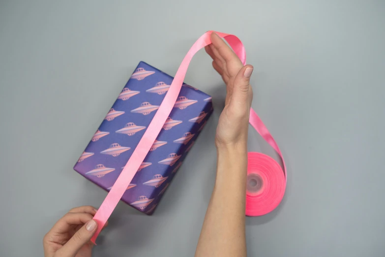 a person wrapping a gift with a pink ribbon, by Rachel Reckitt, dribble, happening, above side view, purple neon colours, close-up product photo, gliding