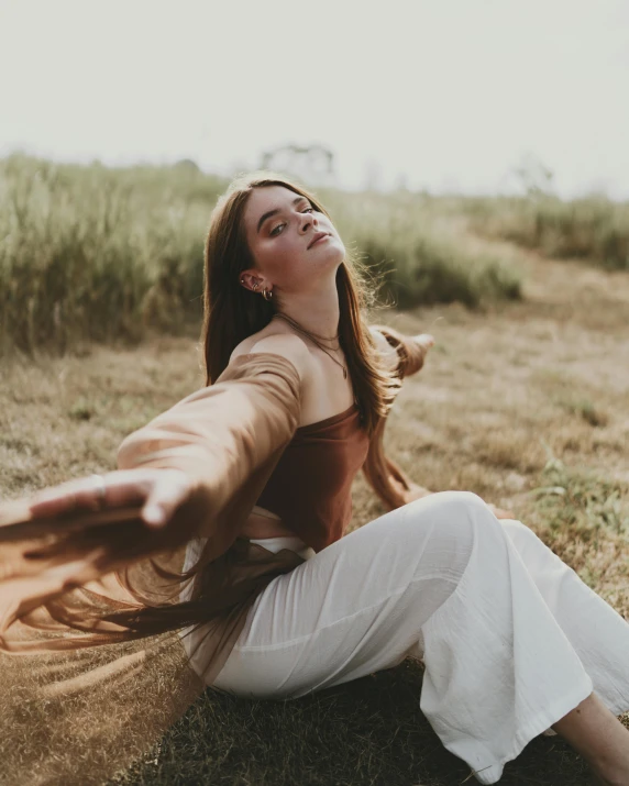 a woman sitting on top of a grass covered field, earthy tones, arms open, non binary model, instagram photo