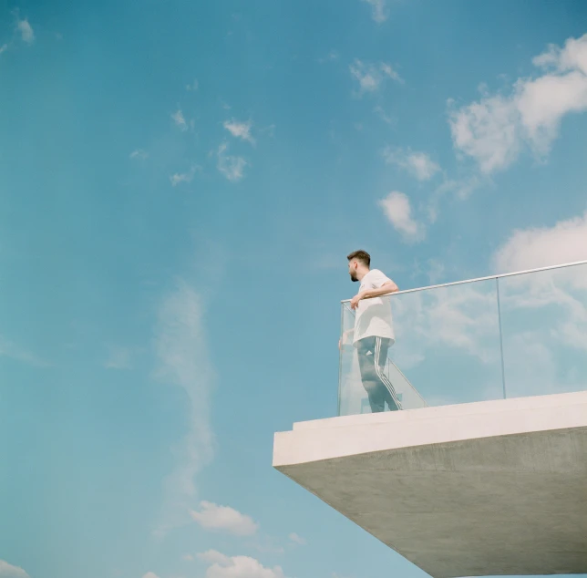 a man standing on a balcony looking at the sky, inspired by Richard Wilson, unsplash contest winner, minimalism, clemens ascher, shot with hasselblad, sky blue and white color scheme, clear glass wall